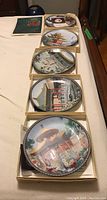 Set of five Chinese Palace Museum collector's plates displayed in boxes, showing intricate colorful designs featuring historical and cultural scenes with traditional Chinese architecture and figures.