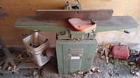 Image showing full Busy Bee jointer woodworking machine with green metal body, red adjustment knobs, and guide fence. Machine rests on solid base with ventilation slots and Busy Bee label.