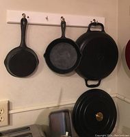Three cast iron skillets hanging on wall rack, along with one cast iron lid on bottom right.