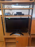 Lot showing Toshiba 26" Regza TV on wooden shelf with remote on shelf below, Sony DVD Player and Liteon DVD Recorder on shelves above, with remotes on top surfaces.