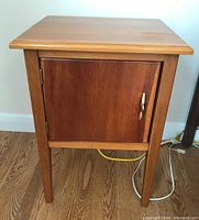Front view of the wooden end table with closed cabinet door showing the metal handle and natural wood finish.