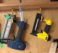 Two pneumatic nailers hanging on wall hooks: blue and black HDC 2 inch finish nailer, yellow and black Power Fist brad nailer.