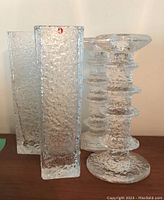 Two clear textured rectangular Linearia glass vases and two textured Festivo glass candlesticks arranged on wood surface