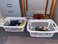 Photo showing white plastic baskets filled with various flashlights and accessories on floor next to filing cabinet