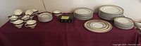 Full view of the dinnerware set on a burgundy tablecloth showing tea cups, saucers, and plates of different sizes.