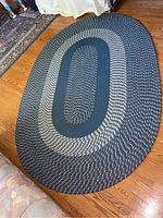 Full view of oval braided area rug placed on wood floor showing overall shape and pattern.