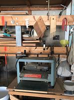 Full view of the planer on a wooden table under a rack holding clamps and feather boards