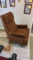 Side view of the mid century recliner showing brown textured fabric, padded arms with wood panels, and recliner lever.