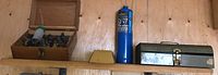 Wooden box with router bits, blue propane cylinder, and small metal storage box on a wooden shelf