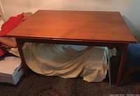 Front view of closed teak dining table showing overall shape and leg design