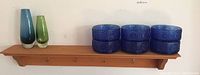 Six blue glass bowls arranged in two stacks of three on a wooden wall shelf.