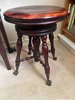 Full view of the vintage wooden piano stool showing round top, turned legs, and claw feet.