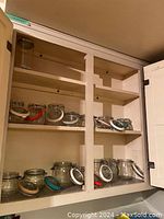 Cabinet shelves containing the set of glass lock top storage canisters showing mostly side view and different shelving levels.