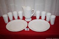 Full set including pitcher, eight glasses, and two plates displayed on table with red cloth.