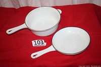 Two white enamel cast iron pieces: saucepan and lid/skillet with handles displayed on red background.