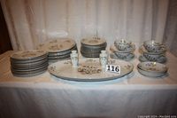 Full set arranged on table showing plates stacked on the left, bowls and salt & pepper shakers to the center right and teacups with saucers stacked at right edge. Oval platter featured in center front.