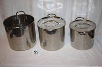 Three stainless steel cooking pots arranged side by side with lids on two smaller pots, largest pot without lid showing inner bottom surface.