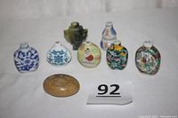 All six Chinese miniature snuff bottles and the painted Chinese-themed rock arranged in a row on a white surface.