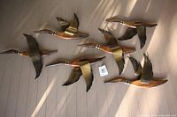 All six flying duck wall decorations displayed on floor showing varied wing positions and spacing, wood and brass materials.