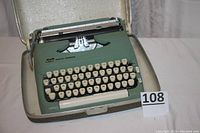 Smith Corona manual typewriter model H65432L with cream-colored keys and green body inside hard case, condition showing use and wear.