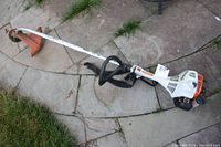 Full view of STIHL FS38 gas powered string trimmer lying on paved surface with grass nearby.