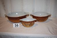 Three brown gradient Pyrex Cinderella style nesting mixing bowls with Old Orchard fruit pattern, shown front and center with lot number tag visible.
