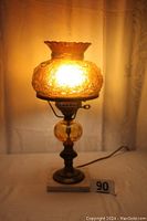 Lit amber glass table lamp showing glowing floral patterned shade and brass base on marble platform.