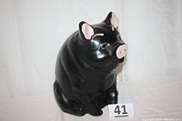 Black chalkware female piggy bank seated facing sideways, showing overall form and finish.