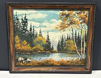 Framed oil on board painting showing a Canadian landscape with lake, trees including birch and evergreens, rocks in foreground under a partly cloudy sky.