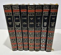 Spine view of the 7 volume set showing black leather spines with gilt and red decorative symbols, titles and authors' names.