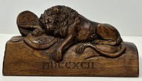 Front view of the wooden carved Lion of Lucerne, showing the reclining lion with shields and Roman numerals on the base.