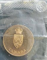 Front side of the gold color Confederation coin showing crown, shield, and 'CANADA' text inside sealed package with star of David.
