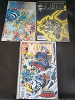 Photo of three comic books: two Xcalibre comics and one Excalibur comic, all in protective sleeves on a dark surface.