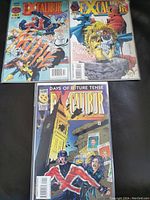 Top-down photo showing three distinct Excalibur comic books with bright, detailed covers placed on a dark surface.