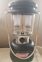 Front view of Coleman outdoor lamp showing black base with Coleman branding and clear globe with two bulb housings.