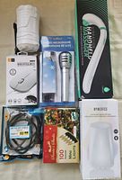 White handheld massager, wired optical mouse, deluxe microphone with stand, HDMI and DP cables, box of 100 mini Christmas lights, HoMedics diffuser visible together on a table.