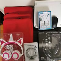 Photo showing three red laptop sleeves stacked, cat ear children's headphones, wireless mouse, Bluetooth earbuds in packaging, black wireless headphones packaging, laptop stand, and white USB cable.