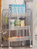 Photo of the mesh rolling cart inside its original box, showing three mesh shelves with various household items placed on them.