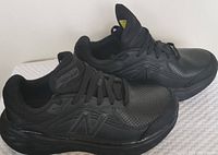 Side view of a pair of women's New Balance black athletic shoes showing leather upper, perforation, and lace-up front.
