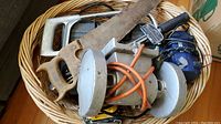 Overview of basket containing assorted tools including hand saws, electric sander, and compressor.