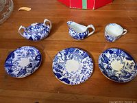 Sugar bowl, creamer, teacup and three blue and white china plates arranged on floor