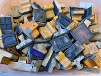 Top view of a plastic container filled with various wood and metal letterpress type stamps showing several letters in upper and lower case and a symbol block.