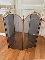 Photo of the fireplace screen fully upright showing four hinged panels with brass edges and mesh center.