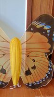 Close-up of the yellow and black patterned butterfly wing with blue details on fabric and yellow central molded body.