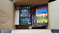 Books packed in a cardboard box showing titles The Camel Club and Redemption.