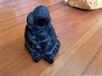Front view of black figurine showing Inuit mother holding child, seated on wooden floor