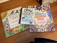 Three main books titled Color Me Happy, Draw 500 Faces and Features, and The Meditation Coloring Book arranged on floor