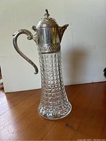 Side view of vintage decanter showing cut glass body and metal top with handle and spout