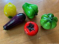 Set of five blown glass vegetables including a yellow lemon, purple eggplant, two green peppers, and a red tomato, all with glossy finish and realistic shaping.