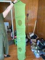 Photo of a person holding a vertical green hanging organizer with 6 compartments, each with circular mesh ventilation holes, in a cluttered indoor room.
